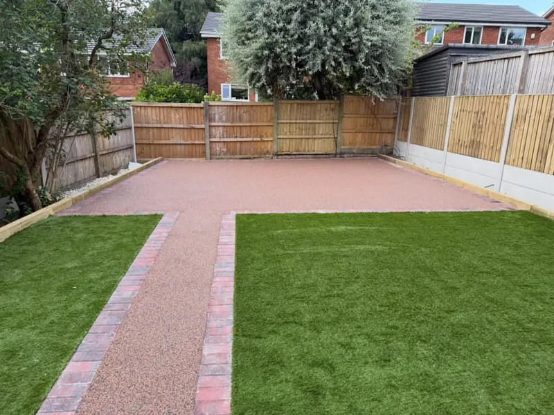 Two sections of artificial grass separated by a tan resin-bound style path and patio, all outlined with multi-coloured brick edging and mixed timber fencing.