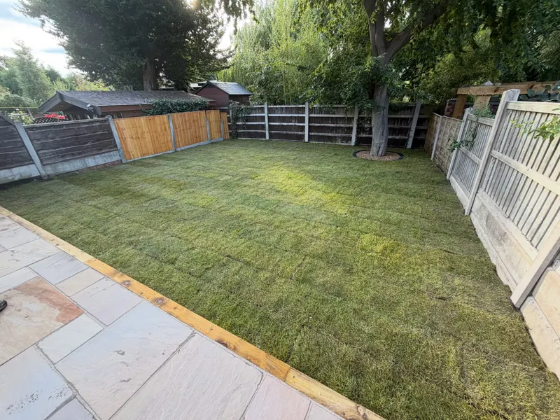Expansive artificial grass lawn with a circular cut-out around a tree trunk, bordered by a timber sleeper edge and mixed wooden fencing.