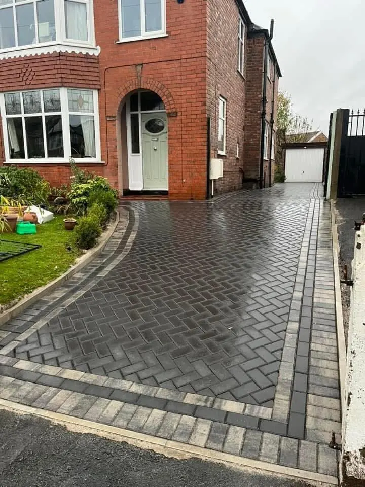Front driveway of charcoal, grey and buff blocks in a herringbone pattern, finished with a dark soldier border along the house, fence lines and pavement edge.