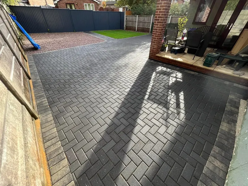 Warm brindle herringbone block paving across a bungalow frontage, centred on three interlinked diamond shapes cut in charcoal blocks and edged with a dark perimeter border.