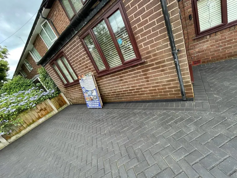 Small rear courtyard paved in red and charcoal brindle herringbone, bordered along a planter bed between white-painted brick walls and black-framed French doors.
