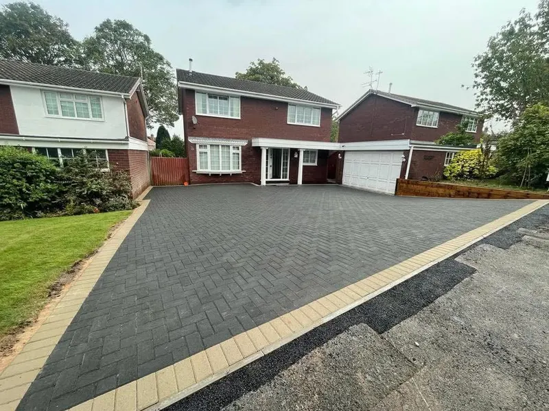 Charcoal herringbone driveway with matching charcoal header border in front of a red brick house, with a linear drainage channel running along the base of the wall.
