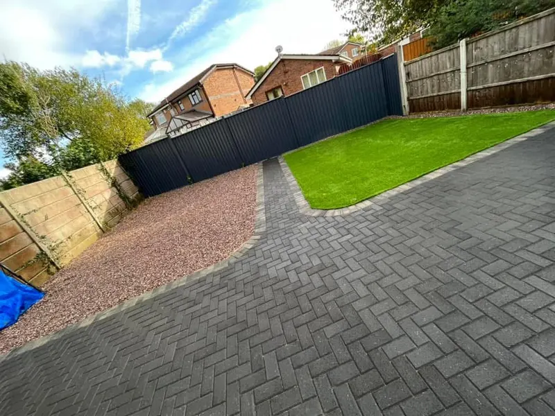 Very large charcoal herringbone driveway spanning a detached red brick house, outlined by a two-course buff border that separates the paving from the front lawn.