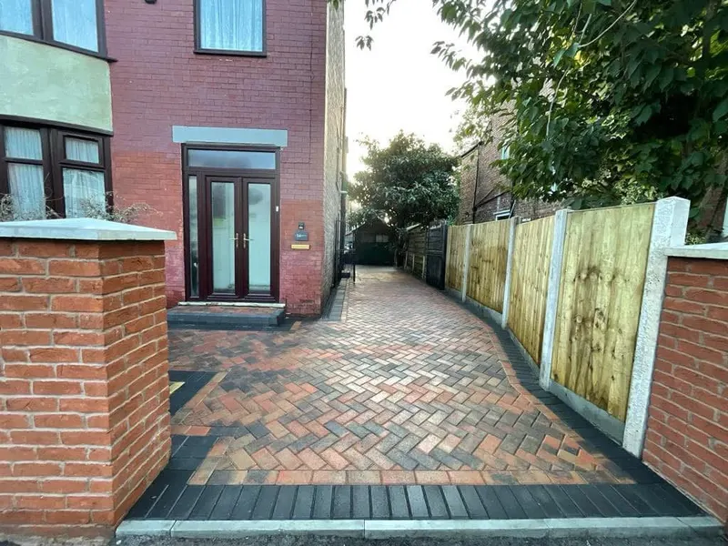 Rear garden layout of charcoal herringbone paving forming a wide forecourt and narrower path, bordered in matching blocks between artificial grass and reddish decorative gravel.