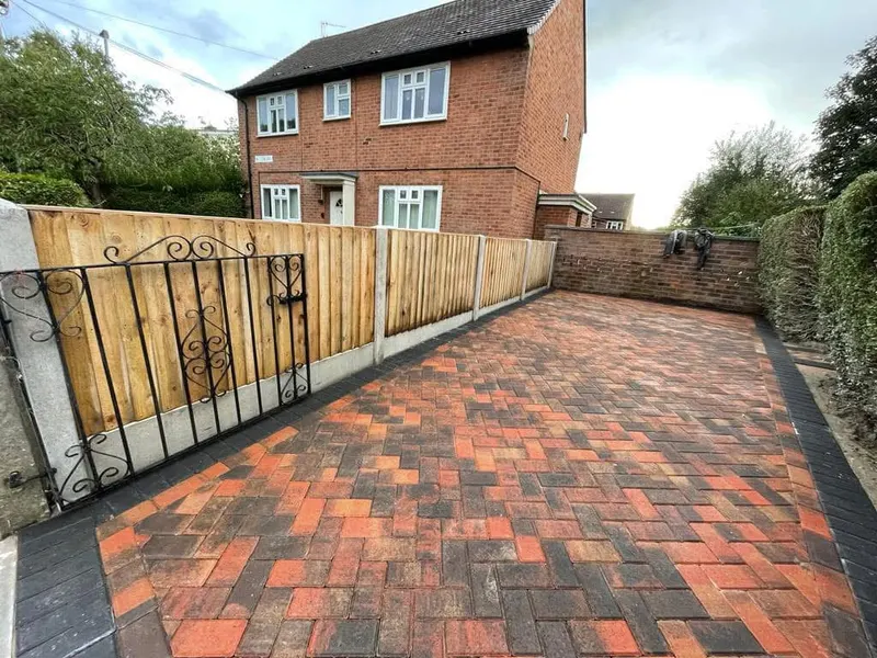 Charcoal block driveway with buff outer border and inner dark accent row before a modern brick house with white garage and front door under gabled roofs.