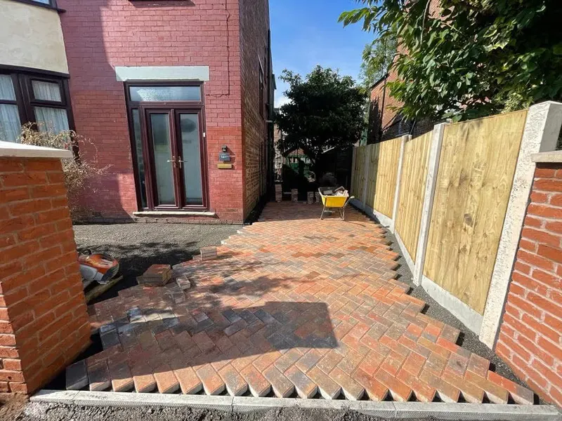 Brindle herringbone paving across a terraced front and under a brick porch, continuing down a side access toward a rear garage with charcoal soldier edging throughout.