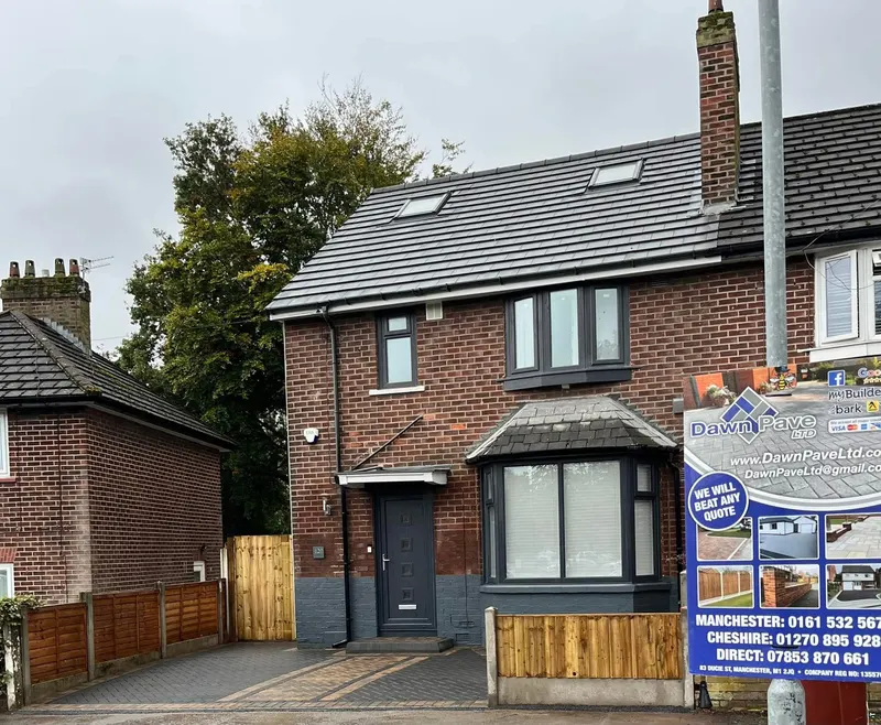 Side access area mid-installation with brindle herringbone blocks laid on grit bedding, stepped uncut edges along a timber fence and brick house with patio doors.