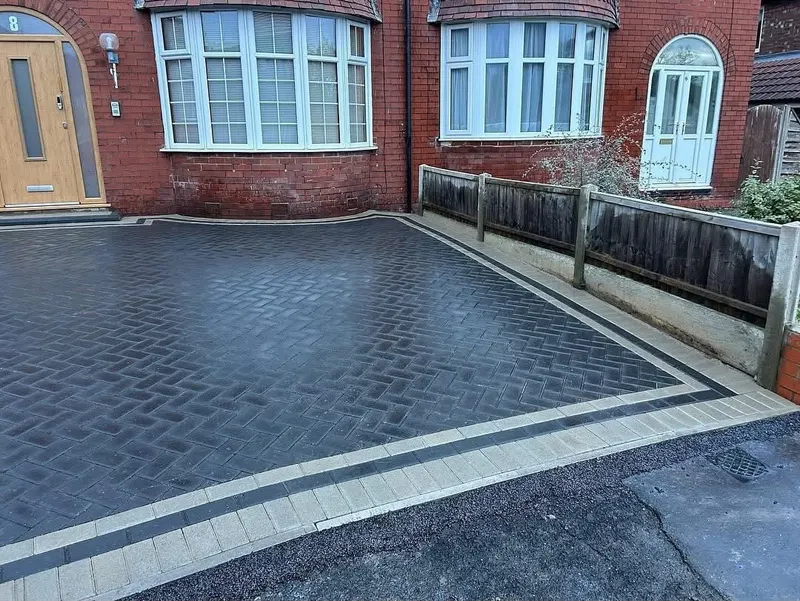 Warm red herringbone driveway and side path with a wide charcoal double border, matching dark edging on a new low brick garden wall beside the house.