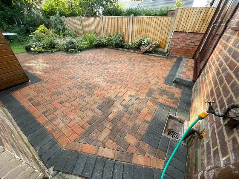 Charcoal herringbone driveway shaped around a white bay window, with a light block double border sandwiched between charcoal courses along the curved edge.
