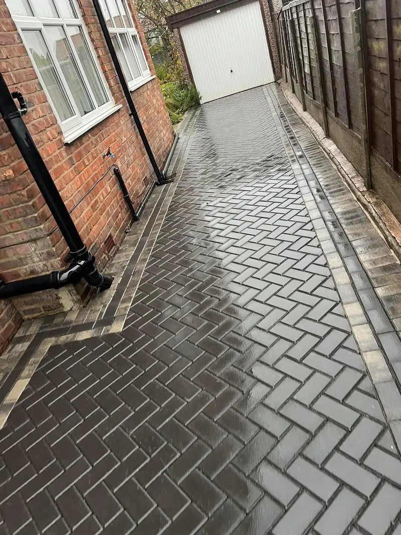 Charcoal herringbone parking area and tan herringbone walkway with double tan borders and charcoal edging, between new timber fences on a red brick house.