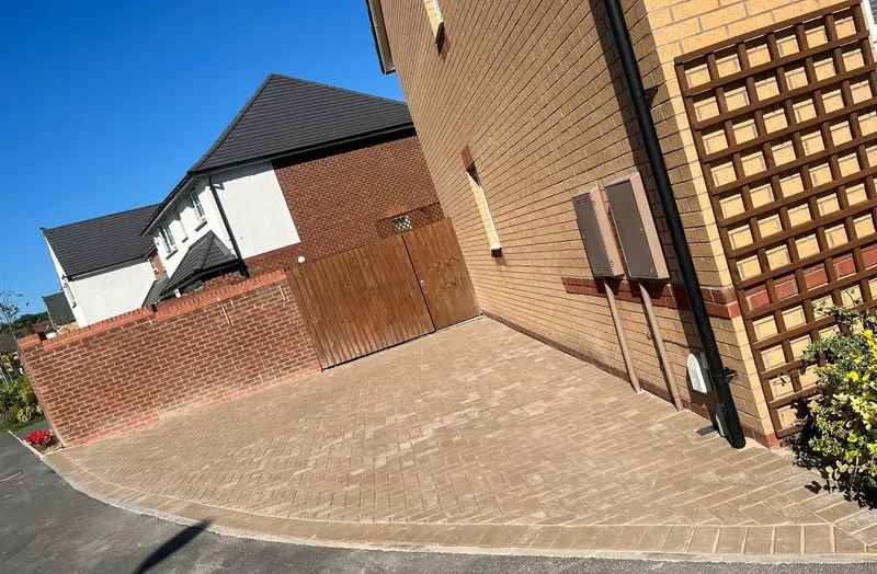 Brindle herringbone driveway and path between house and garage, outlined with a double charcoal border including neat cuts around a utility cover at the edge.