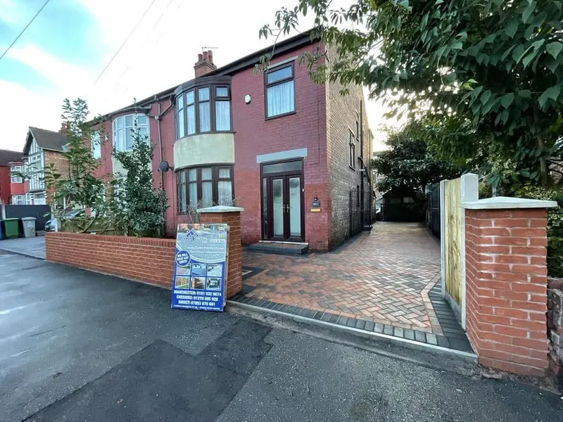 Grey, buff and charcoal herringbone front driveway on a terraced red brick house, with charcoal soldier edging and a slim channel drain at the pavement line.