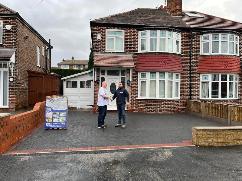 Autumn-toned brindle herringbone driveway and side access on a semi-detached red brick house, framed by a double row of dark charcoal blocks at the kerb and boundaries.