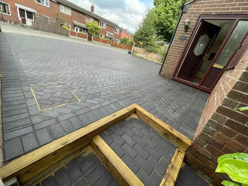 Charcoal herringbone driveway covering a semi-detached front garden, edged along the street with a row of red-toned blocks between low brick walls and fencing.
