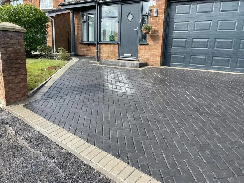 Front layout with tan herringbone path and step bordered in charcoal, flanked by larger charcoal herringbone bays edged in tan header courses toward a grey door.