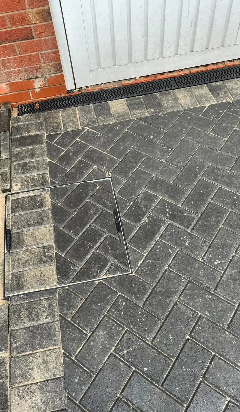 Charcoal herringbone driveway before a grey garage door and matching front door on a red brick house, with a light sand-coloured soldier border along the outer edges.