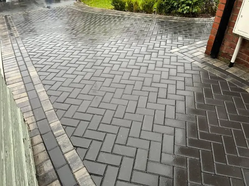 Charcoal herringbone front area and side path framed by alternating charcoal and orange-red border courses, with a raised step topped in red-toned blocks.