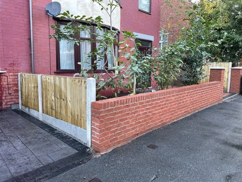 Charcoal herringbone driveway bordered by buff multi-tonal blocks and a black drainage channel on one side, meeting red brick house walls and a front garden curve.