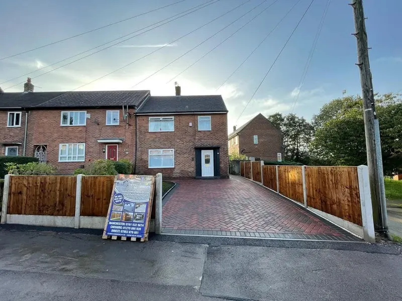 Section of dark grey block paving with charcoal edging next to a new red brick front garden wall and timber fence, in front of a bay-window brick house.
