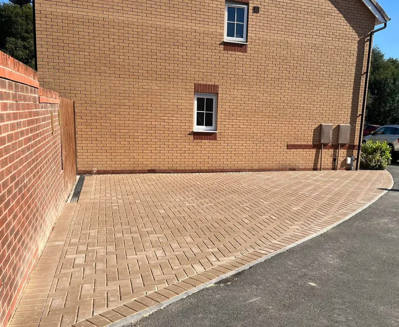 Rear charcoal herringbone patio and wide side path with soldier border, curving beside green lawn and decorative gravel toward a brick porch with a small block step.