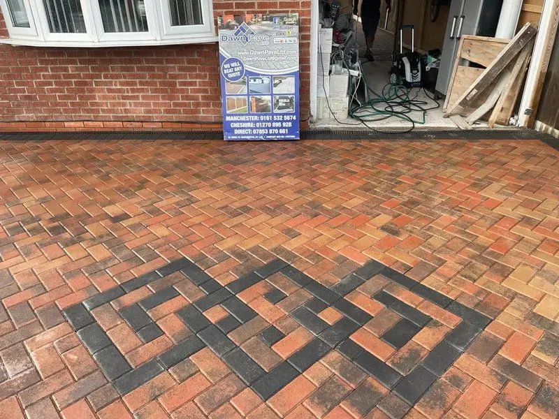 Charcoal herringbone driveway filling a red brick front garden, defined by a perpendicular charcoal header border along the perimeter near garage and front door.