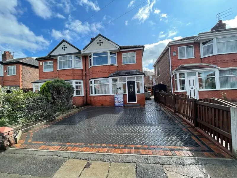 Brindle herringbone front area and long side driveway with charcoal double border, including a matching raised step to brown-framed patio doors beside a panel fence.
