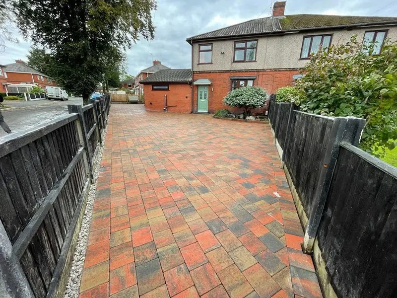 Charcoal herringbone semi-detached driveway with a decorative three-row border alternating red brindle and charcoal blocks along the pavement and property edges.