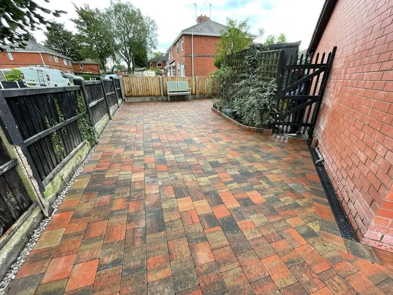 Glossy wet charcoal herringbone driveway with double buff border before a red brick house, with a vehicle parked on the left and timber edging on the right.