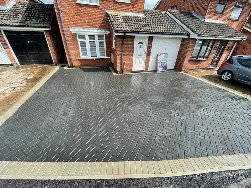 Two-tone block doorstep with buff tread and charcoal riser, opening onto charcoal herringbone drive bordered by buff soldier blocks before a grey composite front door.