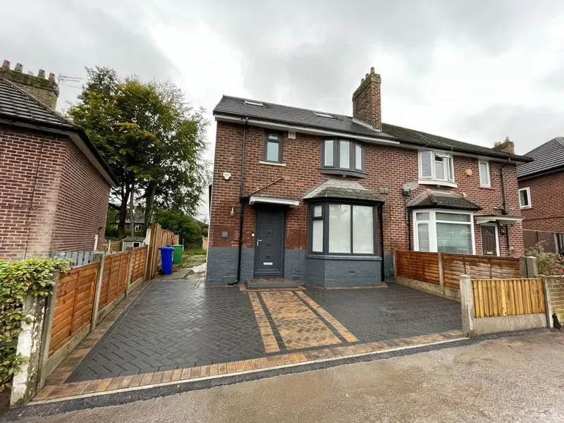 Sheen-finished charcoal herringbone driveway framed in light sandstone-coloured blocks from house to kerb on a red brick property with white garage and door.