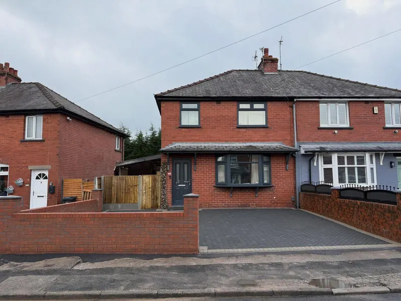 Charcoal herringbone driveway with light grey double border, enclosed by a new red brick wall with dark coping stones and pillars facing a residential street.