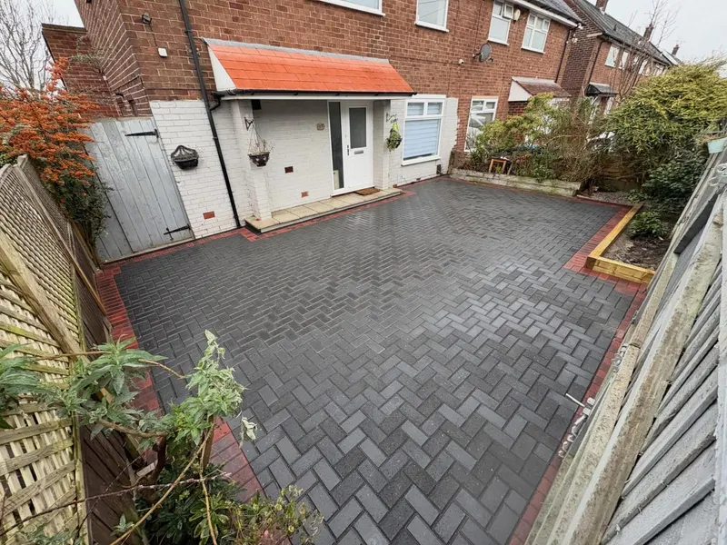 Charcoal herringbone driveway across a red brick semi frontage, with a single row of light blocks along the pavement edge and a low brick boundary wall to the left.