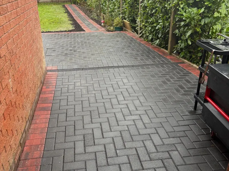 Charcoal herringbone path and step beside a red brick wall, with red soldier border sweeping in a wide curve and a small red diamond inset in the paving.