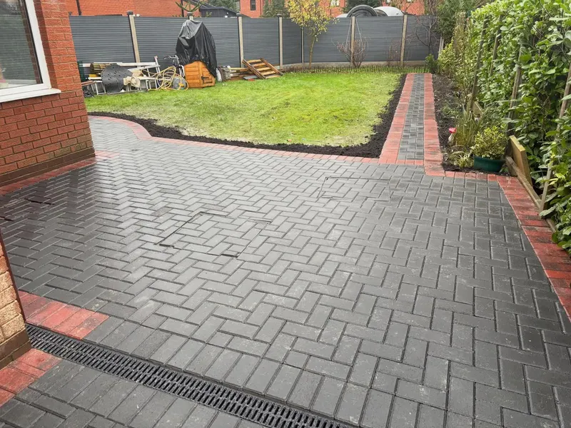 Charcoal herringbone patio with semi-circular double red border and central red diamond detail, plus a matching block step to white French doors on a brick extension.