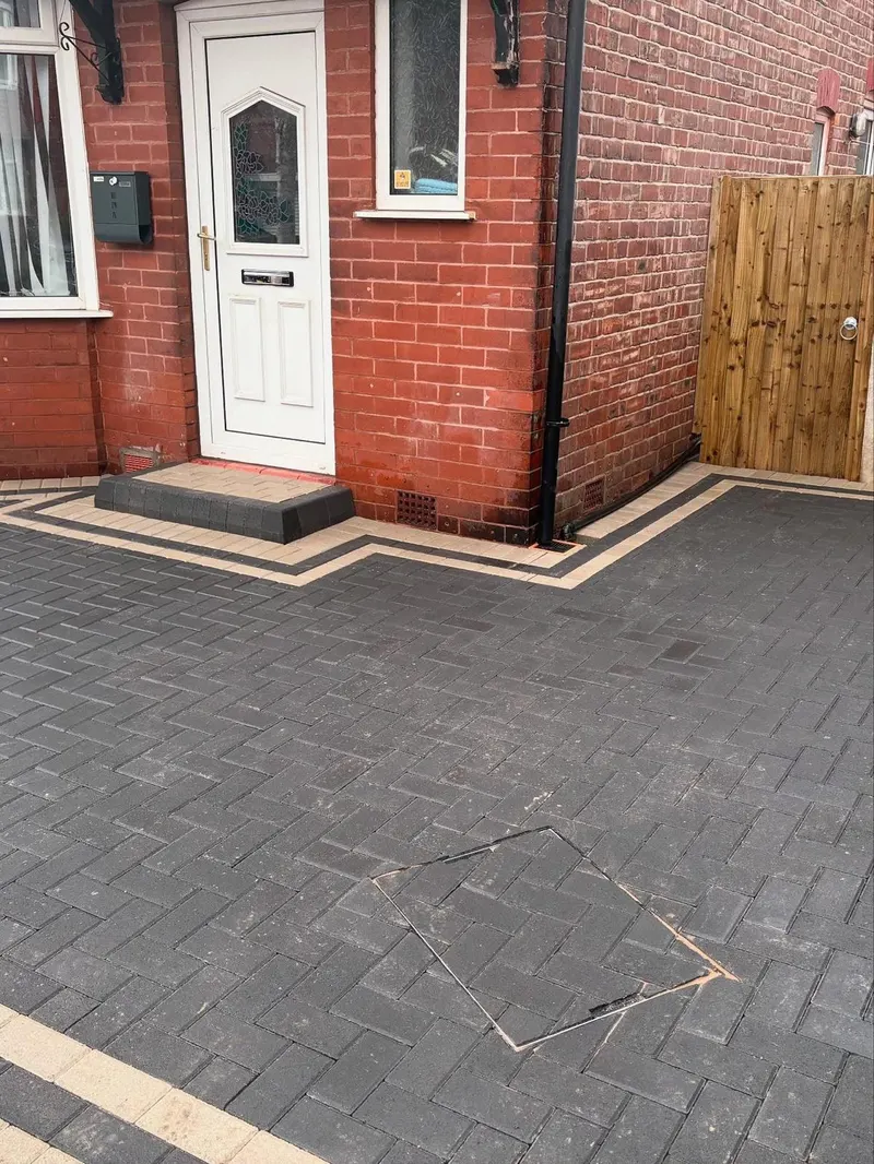Charcoal herringbone driveway and bay window apron with buff double border and inner charcoal soldier course, plus a small block step to a white front door.