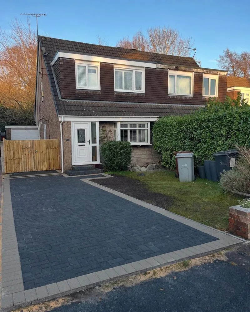 Wide front driveway of red and charcoal brindle block paving with a dark edge course, brick pillars and coping stones in front of a semi-detached house.