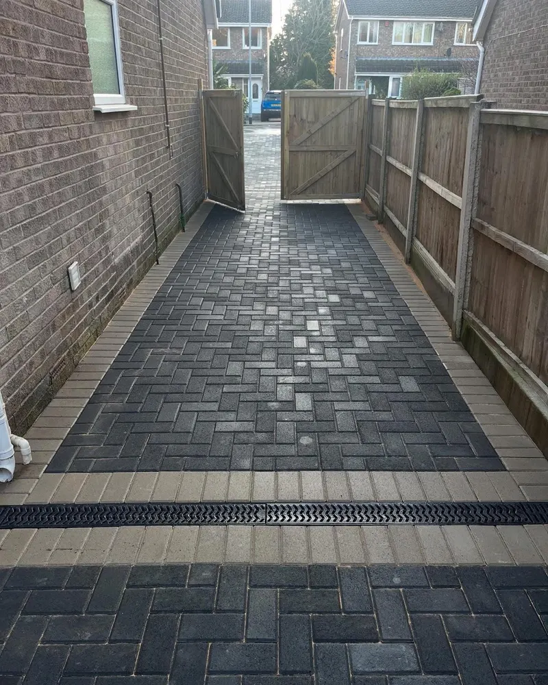 Two raised steps built from charcoal block paving with kerb risers, surrounded by herringbone paving and a cream border at a white door.