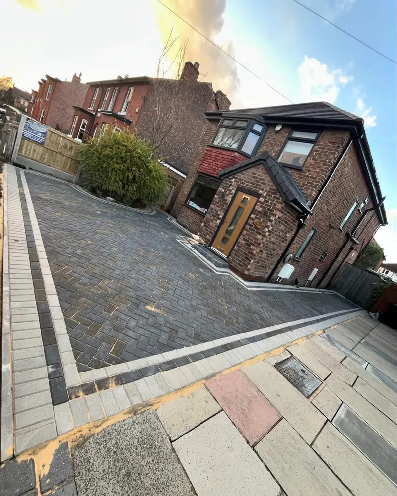 Charcoal herringbone block paving along a brick house with buff borders, tiered steps and a slot drain running to the garage.