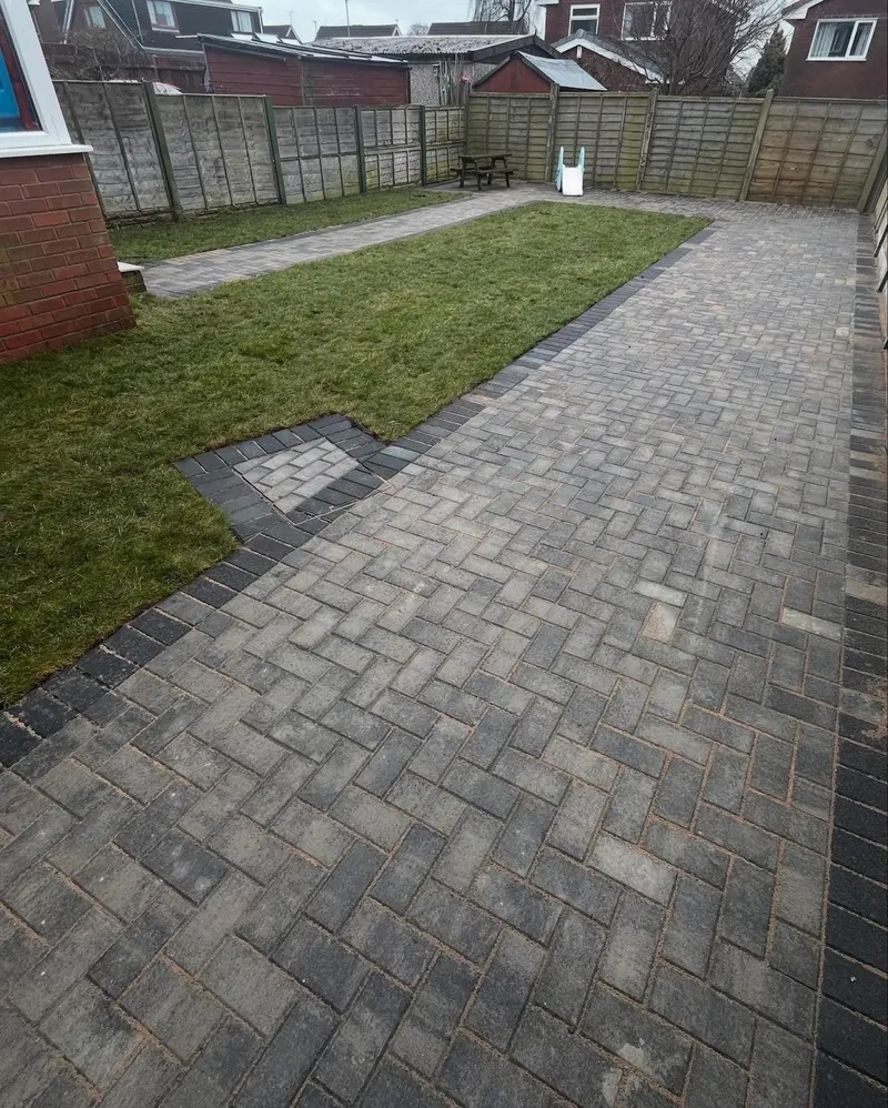Long charcoal herringbone block driveway with double buff borders, wrapping past the front door toward a side garage.