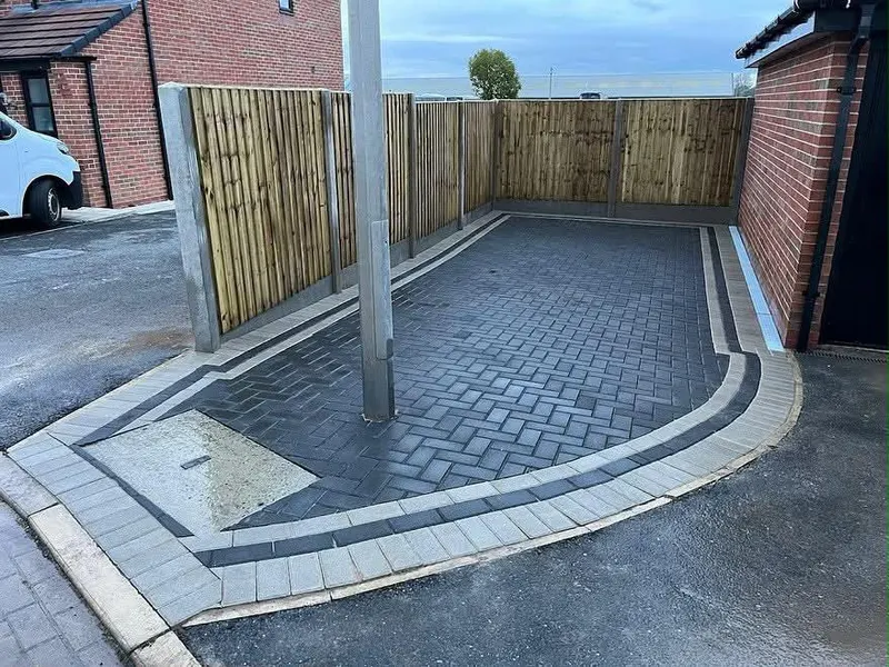 Charcoal herringbone block paving with a terracotta border and matching step, slot drain and hanging baskets on red brick.