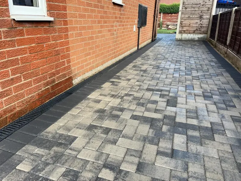 Charcoal herringbone block paving meeting a modern horizontal slat fence, edged with cream and dark triple-row border blocks.