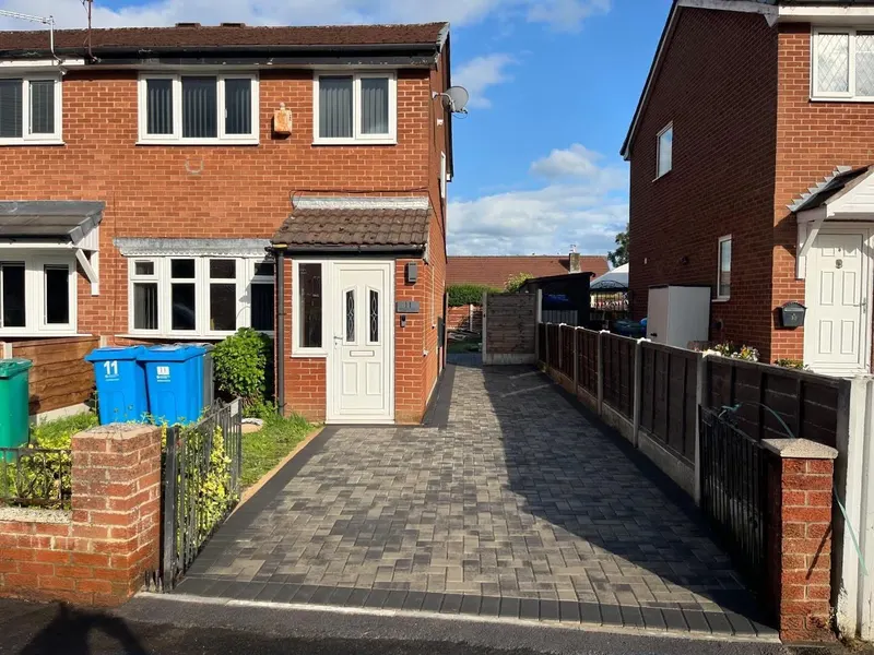Close view of a tray manhole infilled with matching mixed grey block paving so the cover blends with the surrounding surface.