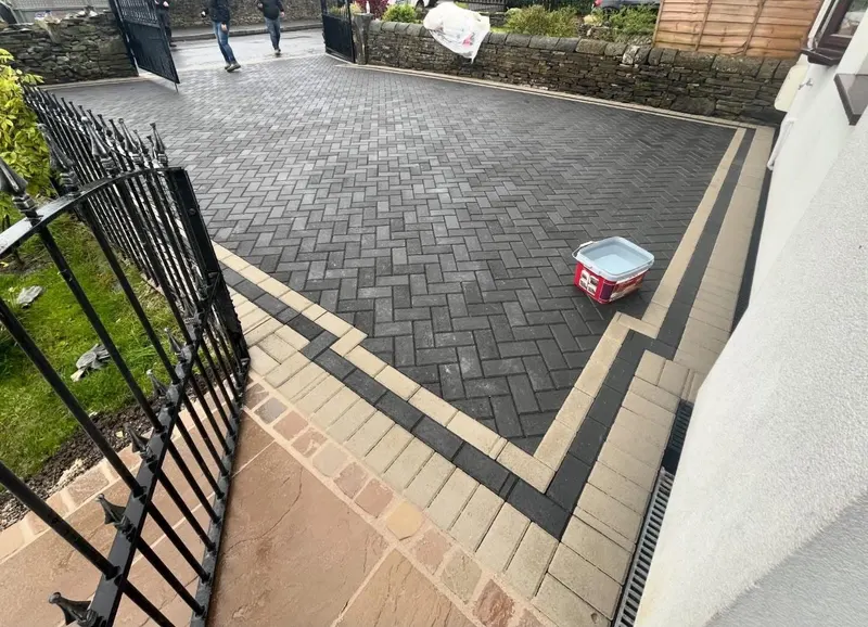 Large charcoal herringbone block patio with silver soldier edging, sweeping past a conservatory and side gate on a brick home.