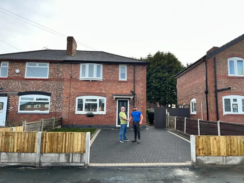 Charcoal herringbone block driveway with a double buff border, integrated lawn panel and soil bed beside timber fencing.