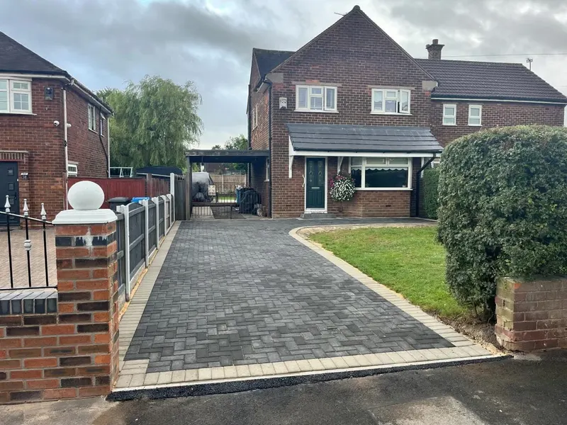 Charcoal herringbone block paving with cream double borders, a built step and drainage gully set against red brick.