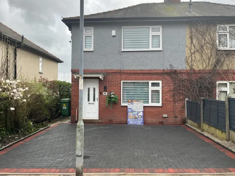 Red and charcoal brindle herringbone block paving with a dark border, slot drain and recessed manhole finished in matching blocks.