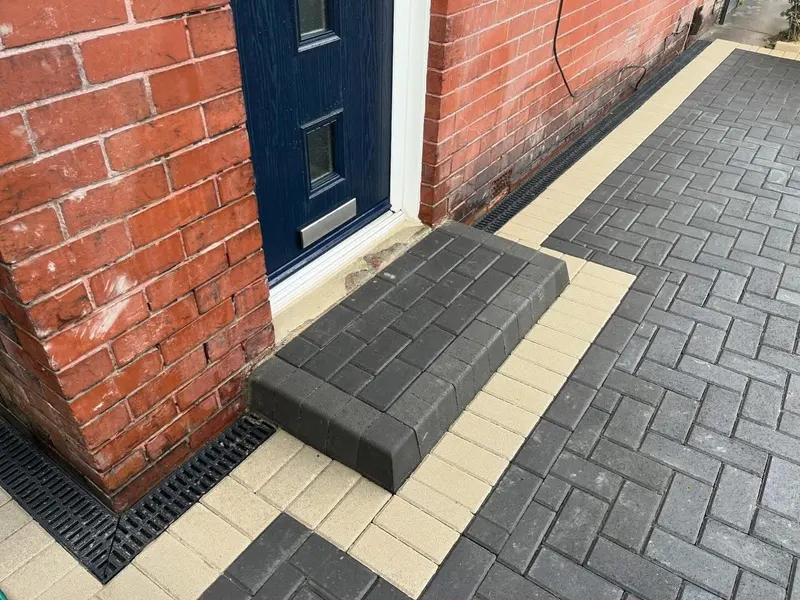 Red and charcoal brindle block paving in herringbone with a dark perimeter border across the front of a two-storey brick house.