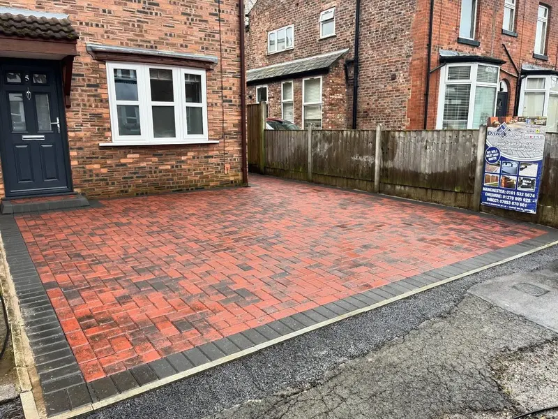 Charcoal herringbone block paving with cream double borders, a raised step and corner slot drain beside a blue front door.