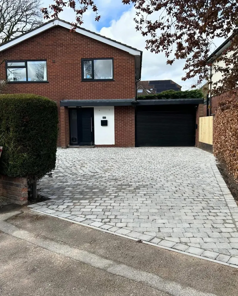 Mixed grey herringbone block paving with a dark-bordered step finished in bullnose kerbs at a cream door on brick.