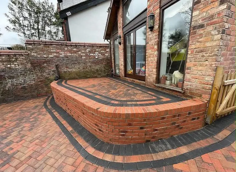 Red brindle herringbone block paving and a single step with heavy charcoal kerb edges leading to a dark grey front door.